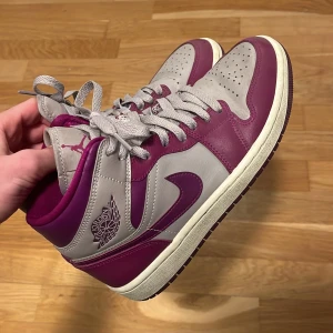 Nike Air Jordan 1 High lila/grå - Nike Air Jordan 1 High sneakers i en snygg kombination av lila och grått skinn. Klassisk Jordan-logga på sidan, perforerad tå och platt sula. Skorna har snörning och en hög siluett som ger en cool vibe. Perfekt för dig som vill sticka ut med dina sneakers. Den högra skon har en defekt färgen har försvunnit lite men märks inte när skorna är på, hör av dig ifall du har npgra tankar eller funderingar!👍PS: inget og följer med