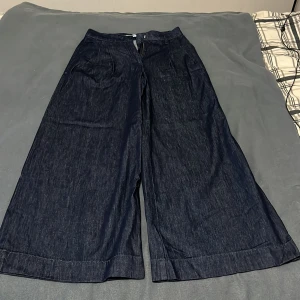 Mörkblå wide jeansbyxor Kappahl 36 - Snygga mörkblå jeansbyxor från Kappahl i storlek 36. Modellen har breda ben och klassisk midja med dragkedja och knapp framtill. Materialet är jeans och byxorna har en loose passform som ger en chill vibe.