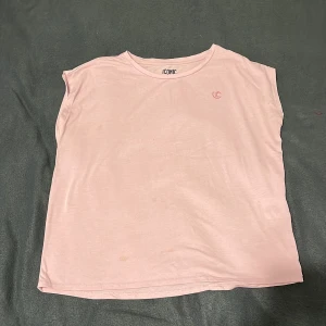 Ljusrosa ärmlös topp från Iconic - Enkel och stilren ljusrosa topp från Iconic i mjuk bomull. Modellen är ärmlös med rund halsringning och har en liten logga tryckt på bröstet. Perfekt för en avslappnad look.