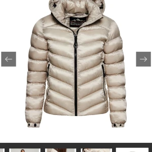 Beige pufferjacka från Superdry - Snygg beige pufferjacka från Superdry med svart dragkedja och huva. Jackan har quiltad design, två fickor med dragkedja och en broderad logga på ärmen. Perfekt för kalla dagar och riktigt skön att bära. Den är aldrig andvänd❤️❤️Dock ingen prislapp kvar men helt som ny, kom privat för fler bilder!