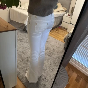 Vita låga jeans - Snygga vita jeans med bootcut och låg midja. Klassisk femficksmodell med silverfärgade knappar och dragkedja. Jeansen har en smickrande passform som sitter tight över låren och släpper ut vid bensluten. Perfekta för dig som gillar en clean och fräsch look.