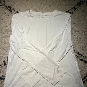 Vit långärmad tröja från Zara - En stilren vit långärmad tröja från Zara i mjuk bomull. Tröjan har en klassisk rund halsringning och enkel design utan mönster eller detaljer. Perfekt för dig som gillar minimalistisk och clean stil.