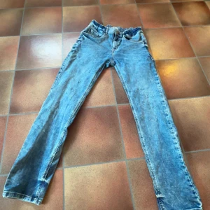 Blå jeans från Lindex, rak modell - Snygga ljusblå jeans från Lindex i rak passform. Klassisk femficksdesign med knapp och dragkedja fram. Jeansen har en cool tvättad look och är tillverkade i bomull. Perfekta för dig som gillar en avslappnad stil. Med slitningar 