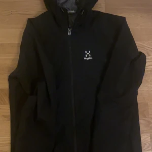 Svart Haglöfs Kaise GTX jacka M - Svart Haglöfs Kaise GTX jacka i storlek M. Jackan har huva, hel dragkedja och minimalistisk design med diskret logga på bröstet. Tillverkad i slitstarkt syntetmaterial och perfekt för blåsiga eller regniga dagar.