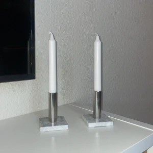 Ljusstakar i marmor  - två fina ljusstakar i metall och marmor. Produkterna har en modern design med fyrkantig marmorfot och cylinderformad metallhållare. Perfekt för stilren inredning. Stearinljusen ingår ej