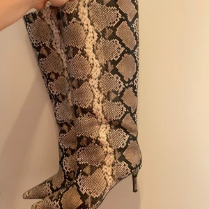 Ormskinnsmönstrade höga stövlar H&M - Ett par coola höga stövlar från H&M:s höstkollektion 2025 i ormskinnsmönster! Superbekväma att gå i och klackskaftet är smalt och ”lagom” högt. Använda under endast 2 månaders tid så skicket är mycket bra. Längst ned på klackarna är det aningen slitet men går enkelt att klacka-om. Storlek 37!🥳🪩