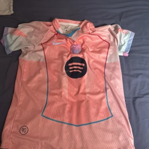 Barcelona Lamine Yamal Nike fotbollströja - Snygg Barcelona fotbollströja med Lamine Yamal och nummer 19 på ryggen. Tröjan är kortärmad, tillverkad i Dri-Fit material och har en ljusrosa bas med blå detaljer, klubbmärke och Nike-logga på bröstet samt Spotify-logga. Perfekt för dig som älskar Barca!