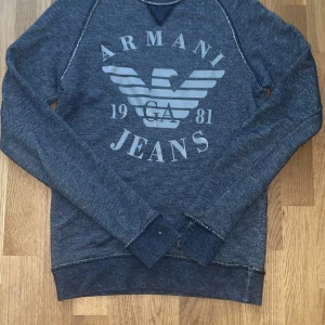 Blå sweatshirt från Armani Jeans - Snygg blå sweatshirt från Armani Jeans med stort logotryck framtill och klassisk rund hals. Tröjan har långa ärmar och mjukt material som passar perfekt till jeans eller joggers. Stilren och enkel design med kontrastsömmar.