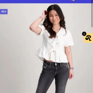 Vit blus med volang och rosett - Supersöt vit blus med volangkant nedtill och rosett framtill. Har lappen kvar och inte använt tog i fel storlek, skriv för bilder