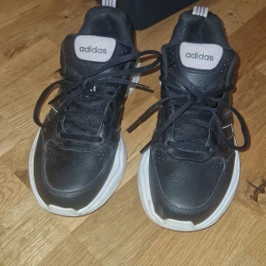 Svarta sneakers - Säljer ett par svarta Adidas sneakers med chunky vit sula och klassisk snörning. Skorna har rund tå och lågt skaft, perfekta för en sportig och avslappnad stil. Inget slitage eller defekter 