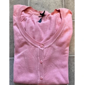 Ljusrosa kofta med knappar - Säljer en ljusrosa kofta från H&M med v-ringad hals och långa ärmar. Koftan har ribbade muddar, två små fickor framtill och stängs med matchande rosa knappar. Perfekt att slänga över en t-shirt eller linne för en chill look.