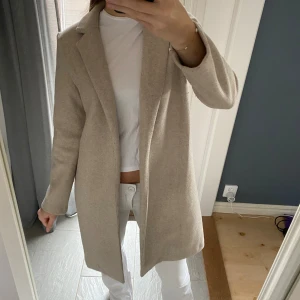 Beige kappa från Zara  - Stilren beige kappa från Zara. Kappan är i mjuk ullmix och i storlek S