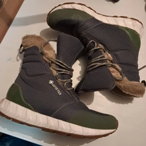 Gröna vinterstövlar ZeroC Gore-Tex - Säljer ett par gröna vinterstövlar från ZeroC med Gore-Tex och fluffigt beige foder. Skorna har snörning, grov sula och detaljer i vitt och olivgrönt. Yttermaterialet är syntet och polyester, perfekt för kalla dagar. Snyggt mönstrad yta och robust design.