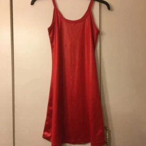 Röd kort klänning med smala axelband - Snygg röd klänning med smala axelband och enkel, rak passform. Klänningen är kort och har en slät yta som ger ett stilrent intryck. Perfekt för dig som gillar minimalistisk design och vill sticka ut med en stark färg.