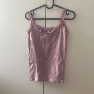 Rosa linnetopp med spets från Isabella - Supersöt ljusrosa linnetopp från Isabella med spetsdetaljer längs axelbanden och urringningen. Toppen är ärmlös och har en mjuk, stretchig känsla som gör den riktigt bekväm. Perfekt att styla med jeans eller kjol för en chill look.