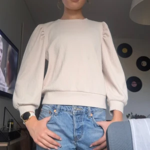 Beige ribbad tröja från JDY - Säljer en beige ribbad tröja från JDY i storlek medium. Tröjan har långärmade puffärmar och bred mudd vid ärmslut och nederkant. Materialet är mjukt och har ett diskret mönster i strukturen som ger en snygg touch till looken.