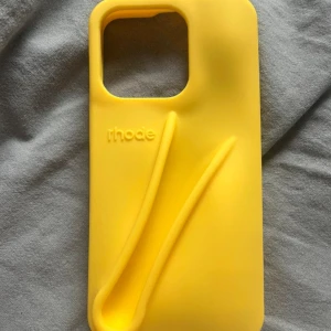 Rhode Lip Case för iPhone - Unik gul Rhode Lip Case för iPhone med integrerad hållare för läppglans. Tillverkad i slitstark silikon, skyddar din mobil och har smart förvaring. Passar utmärkt för dig som vill kombinera stil och funktion. Skick: mycket bra, inga synliga defekter.