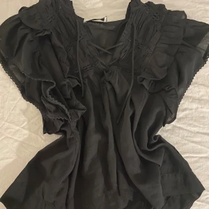 Svart blus med volang från Neo Noir - Supersnygg svart blus från Neo Noir med volangdetaljer och snörning framtill. Aldrig använd! Skriv om ni har frågor! 😊💗