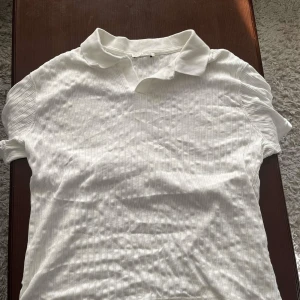 Vit ribbad pikétröja från Zara - Vit pikétröja från Zara i ribbad bomull med klassisk krage och korta ärmar. Enkel och stilren modell som passar perfekt till både jeans och kjol. Snygg struktur i tyget och skön passform för en avslappnad look.