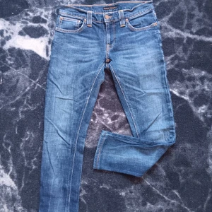 Blå jeans från Nudie Jeans Co - Snygga blå jeans från Nudie Jeans Co med klassisk femficksdesign och kontrastsömmar. Modellen är skinny med smal passform och har en mörkblå tvätt. Jeansen är tillverkade i stretchigt bomullsmaterial för extra komfort och har detaljer som logoknapp och läderpatch bak.