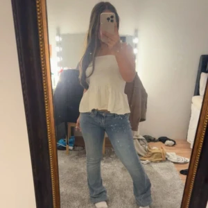 Vit smockad linnetopp med volang - Supersöt vit linnetopp med smockad överdel och volang nertill. Toppen har breda axelband med spetsdetaljer och en luftig, flowy passform. Perfekt för varma dagar och enkel att styla med jeans eller kjol.