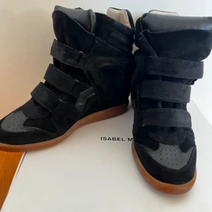 Isabel Marant svarta wedge sneakers - Svarta wedge sneakers från Isabel Marant med högt skaft och platt gummisula i brunt. Skorna har flera kardborreband, rund tå och är tillverkade i mocka och skinn. Den vadderade designen ger en cool och chunky look som sticker ut.Kan skicka mer bilder om det behövs 🥰❤️