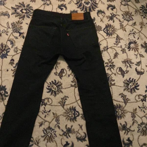 Svarta Levi's Premium 501 jeans - Svarta Levi's Premium 501 jeans med klassisk rak passform och fem fickor. Jeansen har snygga kontrastsömmar och den ikoniska läderpatchen bak i midjan. Tillverkade i slitstarkt bomullsjeansmaterial, perfekt för dig som gillar tidlös stil.