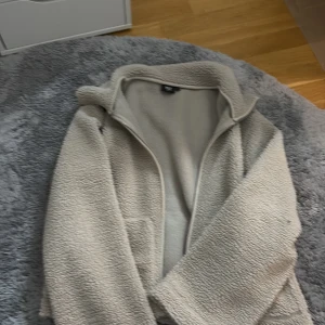 Beige teddyjacka från 157, storlek M - Mysig beige teddyjacka från 157 i storlek M. Jackan har dragkedja framtill och är gjord i fluffigt teddy-material som håller dig varm. Perfekt för kyliga dagar och enkel att matcha med olika outfits.