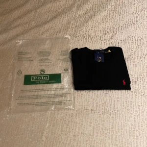 Svart t-shirt Polo Ralph Lauren M - Svart t-shirt från Polo Ralph Lauren i storlek M. Klassisk design med rund hals och korta ärmar, tillverkad i mjuk bomull. På bröstet finns den ikoniska röda Polo-loggan broderad. Perfekt för dig som gillar stilrena och tidlösa plagg.