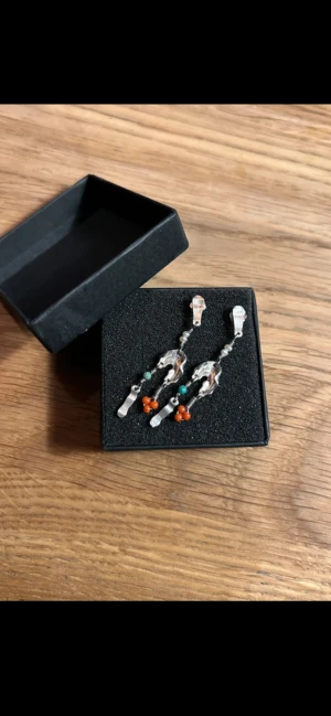 Unika örhängen från Maanesten - Säljer ett par handgjorda örhängen från Maanesten i silver med oregelbundna former, vita pärlor, turkosa och orange detaljer. De har en cool, konstnärlig vibe och sticker verkligen ut med sina mixade material och färger.  Ca 4 cm långa 