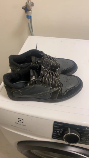 Svarta Nike Travis Scott Jordan  - Säljer ett par svarta Nike Travis Scott jordans Lokontrasterande vita sömmar och broderad logga på hälen. Skorna har snörning, rund tå och platt sula. Ovandelen är i en mix av skinn och mocka, med klassisk perforering på tån och unika detaljer baktill.
