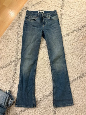 Blå bootcut jeans från Zara, strl 36 - Snygga blå jeans från Zara i storlek 36 med klassisk bootcut passform. Jeansen har fem fickor, dragkedja och knapp framtill. Materialet är slitstarkt denim med lätt tvättad look och kontrastsömmar. Har använts fåtal gånger!