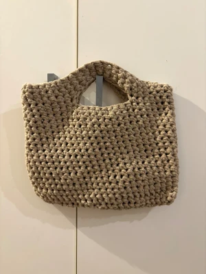 Beige virkad handväska - Säljer en beige virkad väska. Väskan är tillverkad i ett mjukt men hållbart garn som ger en chill och unik vibe. Perfekt för dig som gillar handgjorda accessoarer och vill sticka ut!