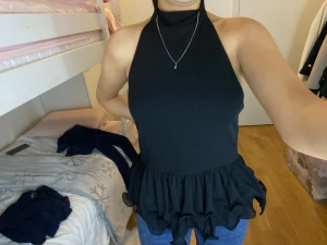 Svart polotopp med volangkant - Säljer en svart polotopp med hög hals och ärmlös design. Toppen har en snygg volangkant nedtill som ger en cool och trendig look. Passformen är normal och materialet känns mjukt och bekvämt, perfekt att styla med jeans eller kjol.