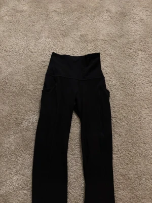 Svarta träningsbyxor från Lululemon -  svarta leggings från Lululemon i storlek 2.med hög midja och praktiska sidofickor. De är tillverkade i ett mjukt och stretchigt syntetmaterial som sitter skönt och följer kroppen. 