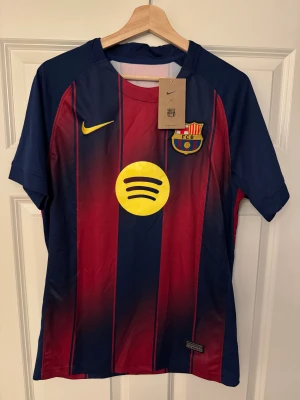 FC Barcelona Lamine Yamal 10 Nike tröja - Säljer en FC Barcelona-matchtröja med Lamine Yamal #10. Kortärmad med klassiska blå/röda ränder, gult Nike-märke och Spotify-logga. Lätt polyester, perfekt för träning eller häng.  Följ oss gärna på Instagram: @kickstoreuf.