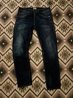 Mörkblå jeans från Abercrombie & Fitch - Snygga mörkblå jeans från Abercrombie & Fitch med klassisk femficksdesign och raka ben. Jeansen har slitningar och tvättade detaljer för en cool look. Passar dig som gillar stilrena och tidlösa jeans med lite edge.