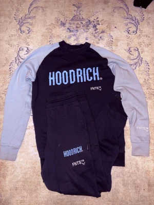 Svart och grå tröja från Hoodrich XS - Nu vill jag sälja min sällsynta Mörk blå tracksuit från Hoodrich i storlek XS med ljus blåa ärmar och tryck på bröstet. Tröjan har långärmad design och är tillverkad i mjuk bomull, perfekt för chill dagar. Snygg kontrast mellan färgerna och coolt FNTS-tryck på ärmen.