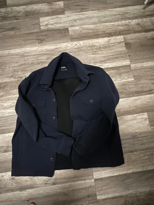 Mörkblå overshirt från Zara - Snygg mörkblå overshirt från Zara med klassisk krage och två stora bröstfickor med knappar. Jackan har långa ärmar och stängs med knappar framtill. Perfekt för lager-på-lager och chill stil.