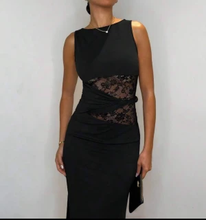 Svart långklänning med spetsdetalj - Supersnygg svart långklänning med transparent spets i midjan och omlott-detalj. Klänningen är ärmlös och har en tight passform som framhäver figuren  frakt står inte jag för