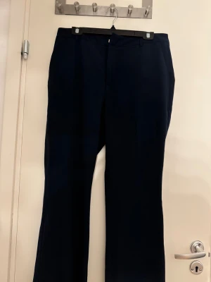 Mörkblå kostymbyxor med wide fit - Snygga mörkblå kostymbyxor med klassisk wide fit och raka ben. Byxorna har midwaist, bälteshällor och diskret dragkedja framtill. Perfekt för dig som gillar stilrena och enkla plagg med lite extra attityd.