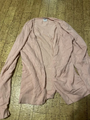 Ljusrosa kofta från Saint Tropez - Säljer en ljusrosa, tunn och öppen kofta från Saint Tropez i storlek M. Koftan har lång ärm och är tillverkad i mjukt stickat material. Perfekt att slänga över en t-shirt eller linne för en chill look.