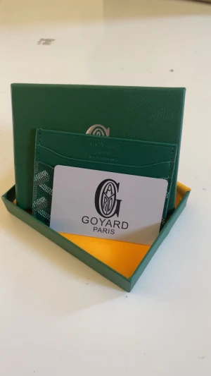 Grön korthållare med mönster - Snygg grön korthållare med ikoniskt grafiskt mönster i vitt och grått. Slimmad design med flera fack för kort, tillverkad i exklusivt skinn. Kommer med original ask och gul putsduk, perfekt för dig som gillar lyxiga accessoarer.