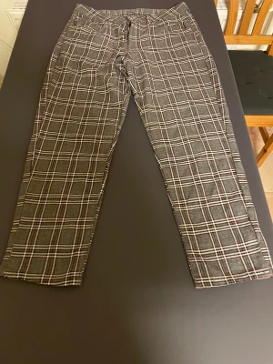 Rutig kostymbyxa från Vailent, storlek L - Snygga kostymbyxor från Vailent i storlek L med grå, svart och vit rutig design och inslag av vinrött. Klassisk rak passform och midwaist. Perfekt för dig som gillar en stilren och trendig look. Materialet känns som en mjuk blandning av bomull och syntet.