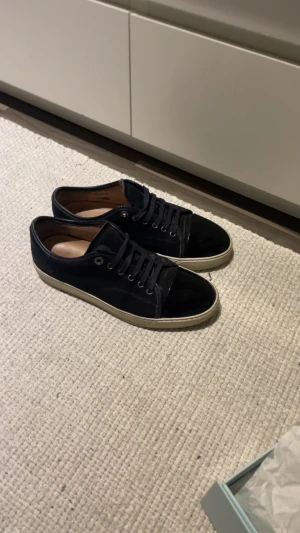 Byte lanvins  - Lanvin sneakers i svart mocka med glansig tå och vit platt sula. Klassisk rund tå och snörning framtill. Snygg och stilren design med exklusiv känsla, levereras med originalkartong och dustbag. Perfekt för dig som gillar lyxiga detaljer och fransk mode.