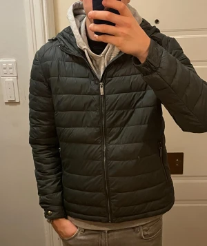 Jacka | Massimo Dutti - Grön pufferjacka från Massimo Dutti med quiltad design och huva. Jackan har dragkedja framtill, sidofickor med dragkedja och en snygg knappdetalj vid ärmslutet med logga. Lättviktig och vattenavvisande, perfekt för kyliga dagar.