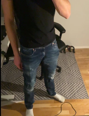 Snygga jeans - Säljer ett par snygga jeans i mörkblå tvätt med  färgstänk och slitningar på benen. Passformen är slim.  Personen på bilden är 180 