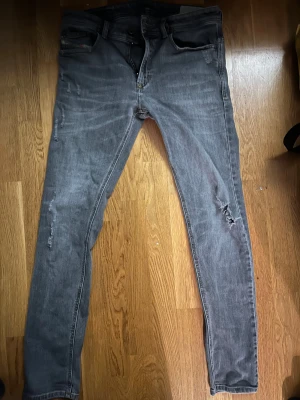 Grå Diesel Larkee jeans skinny fit - Snygga grå jeans från Diesel, modell Larkee, med skinny passform. Jeansen har slitna detaljer på benen och klassisk femficksdesign. Perfekta för dig som gillar en smal siluett och en lite ruffare look.