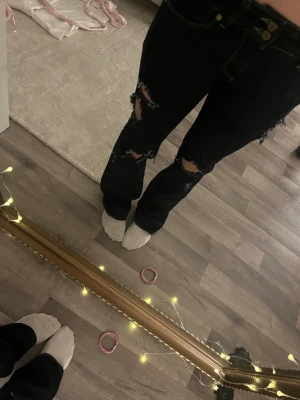 Svarta ripped jeans med wide fit - Säljer ett par mörka jeans med breda ben och snygga slitningar på låren och knäna. Jeansen har klassisk femficksdesign, kontrastsömmar och dubbla metallknappar i midjan. Perfekt för dig som gillar en avslappnad och trendig look. Köptes i usa har storlek 25