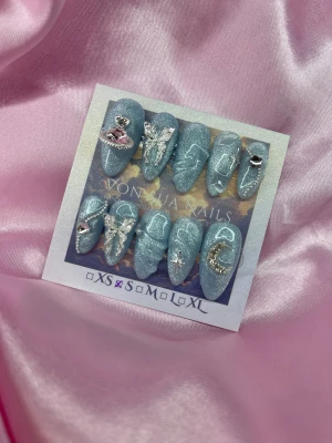 Yuki (S);Medium Almond - Set med handgjorda press-on naglar i glittrigcateye blått med silverdetaljer. Naglarna har coola 3D-charms som fjäril, måne, stjärna och hjärta, samt vita linjer som ger en dreamy vibe. Formen är medium almond. Perfekt för dig som vill ha unika och trendiga naglar.S: 15 mm, 11,5 mm, 12 mm, 11 mm, 9 mm 